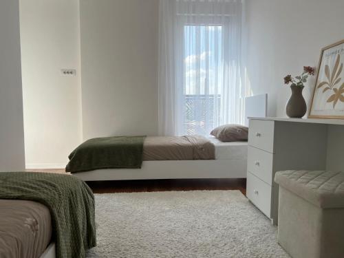 a white bedroom with two beds and a window at Nil Apartment - Free Parking in Pristina