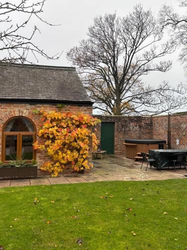 Courtyard House- Luxury Holiday House with floodlit Tennis court في نورثاليرتون: مبنى من الطوب مع شجرة بأوراق الخريف