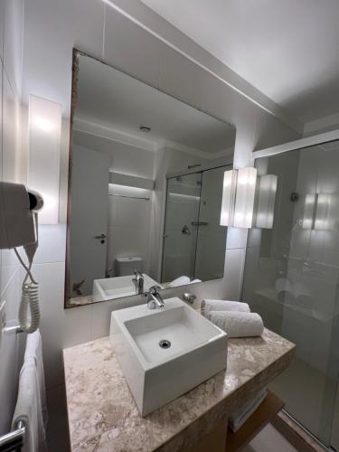 a white bathroom with a sink and a mirror at Flats na praia com AC, piscina, sauna e academia! in Santos