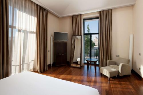 a hotel room with a bed and a chair and window at NH Collection Palacio de Aranjuez in Aranjuez