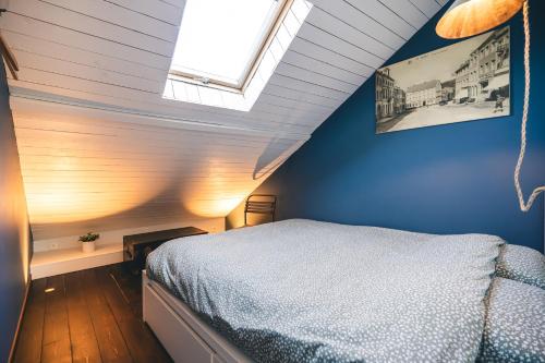 1 dormitorio con 1 cama con pared azul y ventana en L'Atelier - Gîte chaleureux et relaxant, en Saint-Hubert