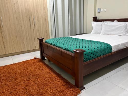 a bedroom with a bed with a green blanket and a rug at Beatrice court in Accra