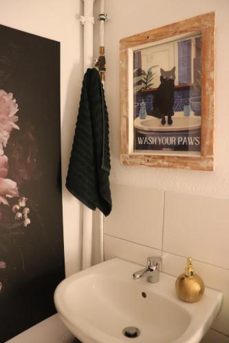 a bathroom with a sink and a picture of a black cat at Hostel Bertha-Marie Flamingo Lounge in Greifswald