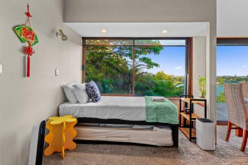 ein Schlafzimmer mit einem Bett und einem großen Fenster in der Unterkunft Tranquil West Haven with Water and Skyline Views in Auckland