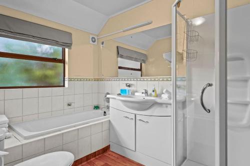 ein Badezimmer mit Waschbecken, Badewanne und Toilette in der Unterkunft Tranquil West Haven with Water and Skyline Views in Auckland