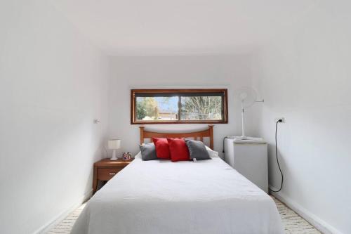 a bedroom with a white bed with red pillows at Lakeside Getaway Halekulani in Budgewoi