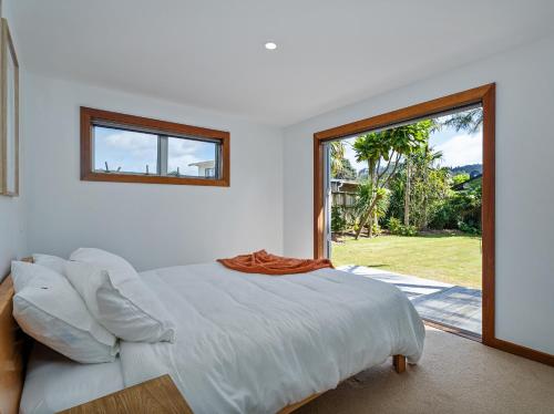 a white bedroom with a bed and a large window at Summer Palms - Tairua Holiday Home in Tairua