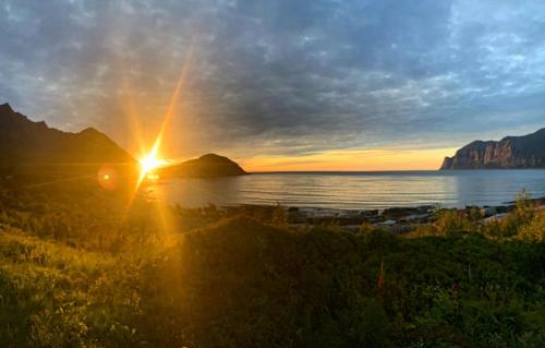 a sunset over a body of water with the sun shining at Solstad in Senja