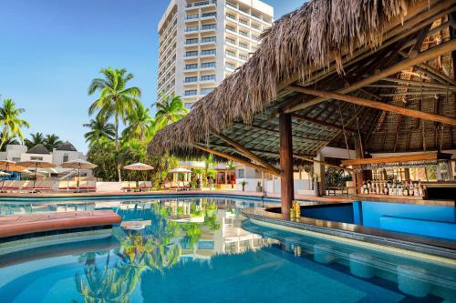 a swimming pool at a resort with a thatch roof at Sunscape Dorado Pacifico Ixtapa Resort & Spa- All Inclusive in Ixtapa