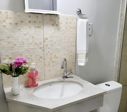 a bathroom with a sink and a vase with a pink flower at Sobrado 6 amplo e confortável em condomínio in Corumbá