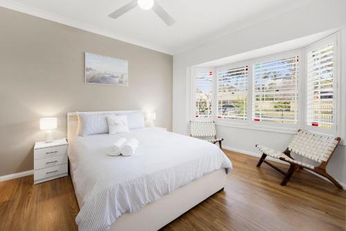 a white bedroom with a white bed and two windows at Dolphin Cove - Pet Friendly with Fireplace in Callala Bay