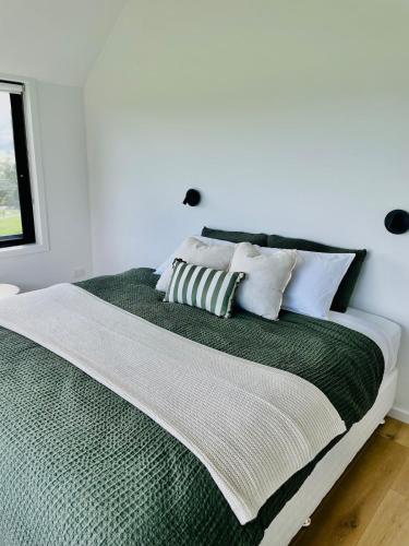 a white bedroom with a green bed with white pillows at NEW Luxury Cabin with Scenic Views & Farm Charm in Huonville