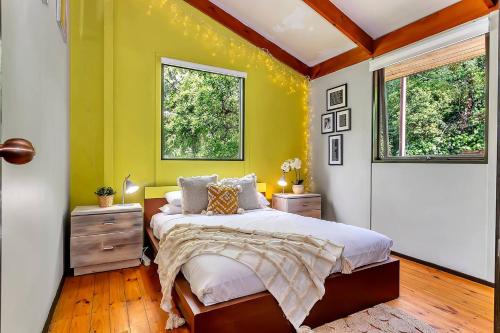 ein Schlafzimmer mit einem Bett mit gelben Wänden und Fenstern in der Unterkunft Treetop Sanctuary - Serene Cottage near Mount Lofty in Upper Sturt