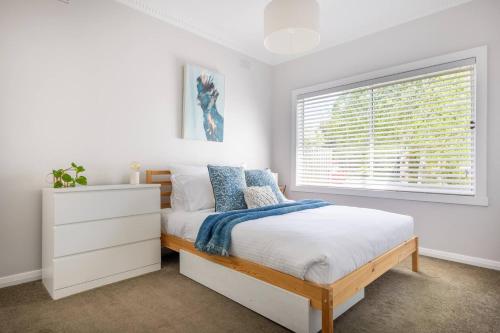 a white bedroom with a bed and a window at Oaklight Haven - Minutes to Geelong Waterfront & CBD in Hamlyn Heights