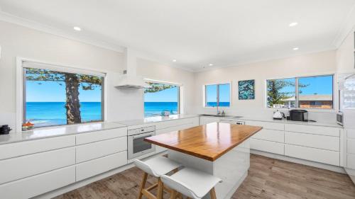 a kitchen with white cabinets and a wooden table at Beachfront Breeze - Family Getaway By Holidayco in The Entrance