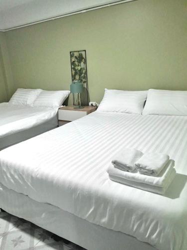 two beds in a bedroom with white sheets and towels at 113 Yellow House Hostel in Phuket