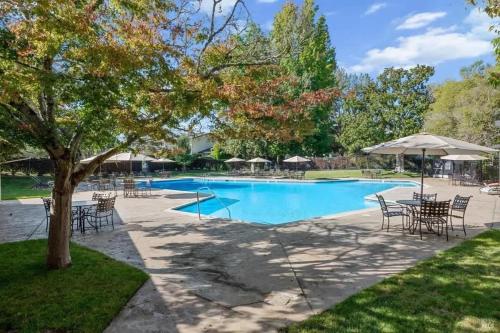 una piscina con mesas, sillas y un árbol en Luxe Golf View Condo Prime Napa Location, en Vichy Springs