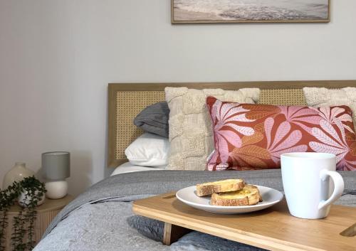 a plate of toast on a wooden tray on a bed at The Little Beach Retreat - Relaxing family sized home one street from the sea! in Port Willunga