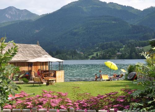 a group of people sitting under an umbrella near a lake at Ferienhaus Knaller in Weissensee