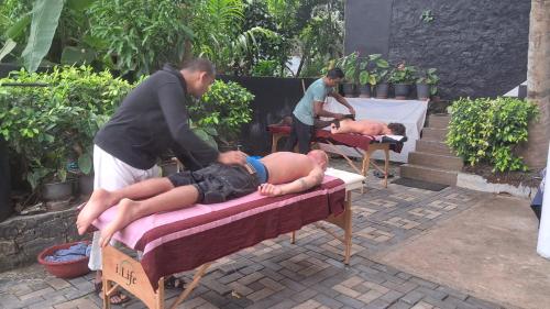 Ein Mann lag auf einem Bett, zwei Männer standen um ihn herum. in der Unterkunft Indunil Family Residence With Pool Hiriketiya in Dikwella