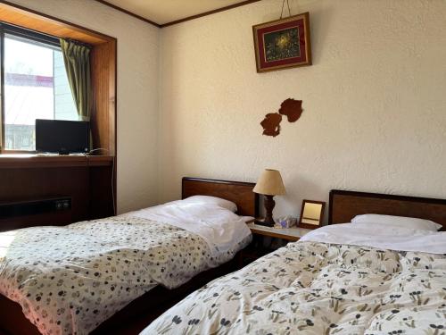 a bedroom with two beds and a tv on the wall at ペンションとも in Nosakada