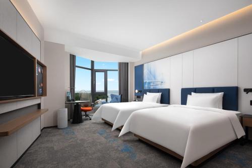 a hotel room with two beds and a flat screen tv at 海口国贸希尔顿欢朋酒店 in Haikou