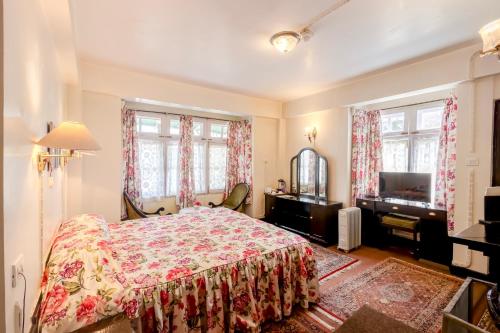 a bedroom with a bed and a tv and windows at Windamere Hotel - A Colonial Heritage Since 1841 in Darjeeling