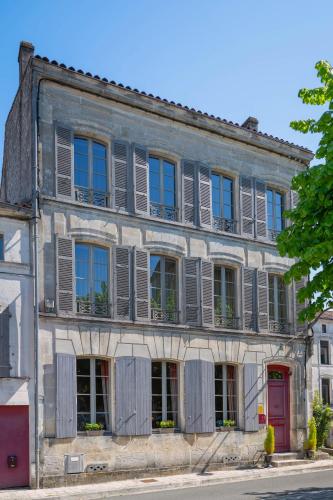 an old building with gray shutters and a red door at Hotel Ligaro - Jarnac in Jarnac