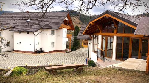 a white house with a wooden roof and a bench at Pensiunea Casa-Stefanel in Sadova