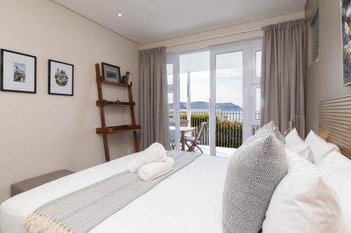 ein Schlafzimmer mit einem großen weißen Bett und einem Balkon in der Unterkunft Dorian Place Oceanview Getaway in Simon’s Town in Murdoch Valley