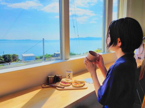 a woman sitting at a table holding a coffee cup at 「淡路島一棟貸宿　野うさぎ 」高台から海を望む貸別荘！2023年新築離れの素泊まり in Noda