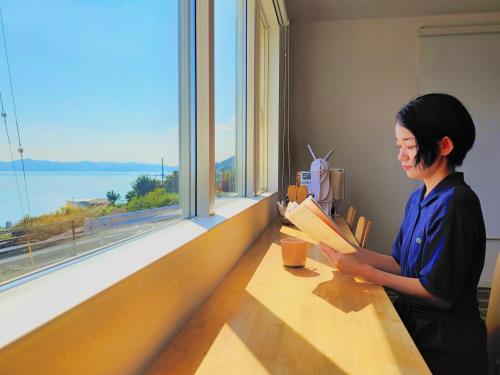 a woman sitting at a table reading a book at 「淡路島一棟貸宿　野うさぎ 」高台から海を望む貸別荘！2023年新築離れの素泊まり in Noda