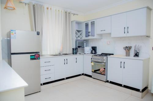 a white kitchen with white cabinets and a refrigerator at A Beautiful home, Kanombe, Nyarugunga in Kigali