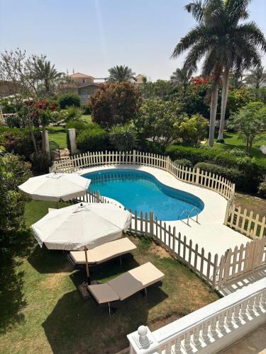 a pool with umbrellas and chairs and a fence at Akasha Villa in Madīnat ash Shurūq