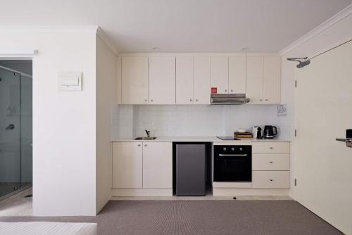 a kitchen with white cabinets and a black dishwasher at Queen Bed Studios with Sofa at Manly - 3min walk to Corso & Manly Beach in Sydney