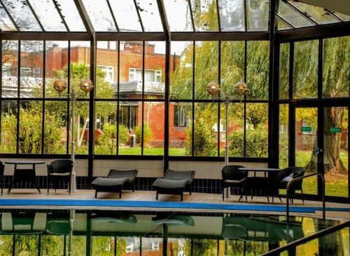 a swimming pool with chairs and tables in a building with windows at Brook Mollington Banastre Hotel & Spa in Chester