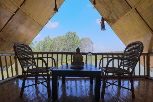 een standbeeld zittend op een tafel op een veranda met twee stoelen bij The Buddha Village in Chik Ballāpur