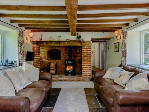 ein Wohnzimmer mit Ledersofas und einem gemauerten Kamin in der Unterkunft Eton Cottage in Farnham