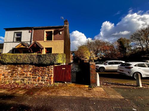 a house with a red gate and cars parked in a parking lot at Squirrel Cottage in Stoke on Trent