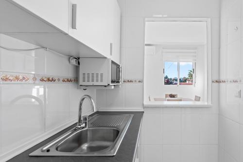 een witte keuken met een wastafel en een raam bij Pleamar 23 in Torrevieja