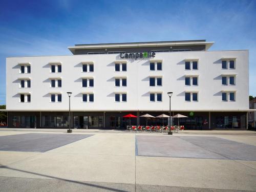 a large white hotel with tables and umbrellas in front of it at Campanile Ales Centre - Cévennes in Alès