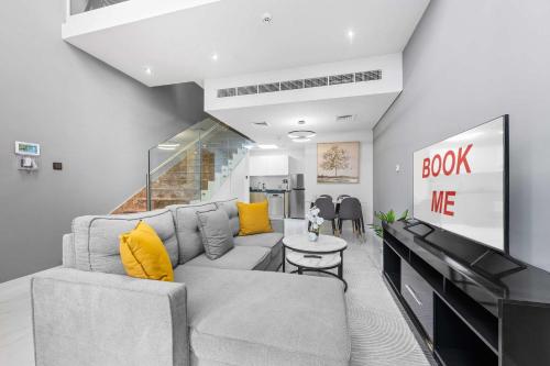 un salon avec un canapé gris et des coussins jaunes dans l'établissement StayShort - Cozy 1BR Townhouse loft style located in Rukan Community, à Nadd Shubayḩ