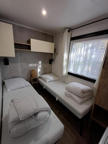 two beds in a small room with a window at Mobil home 6 personnes 3 chambres in Pont-Aven