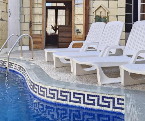 a group of white lounge chairs next to a swimming pool at Sunset Castle House with Pool in Xagħra