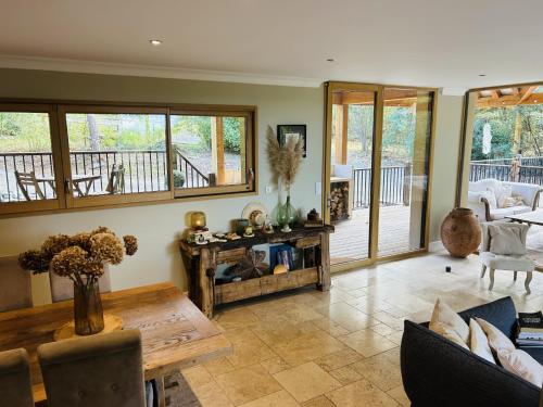 a living room with a wooden table and a porch at Villa Nature & Douets - aux portes du Mans - 5 chambres climatisées - piscine à débordement et terrain arboré d'1 hectare in La Chapelle-Saint-Aubin