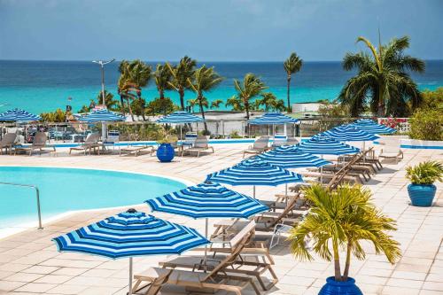 a pool with blue and white umbrellas and chairs and the ocean at Royal Islander Club Resort La Terrasse in Lowlands