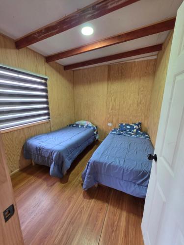 two beds in a small room with wood floors at Cabaña Playa Chauquen in Neltume
