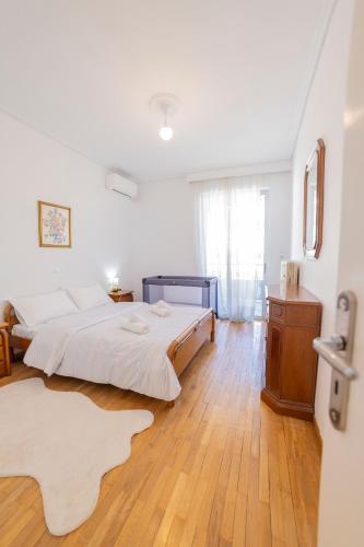 a white bedroom with a bed and a wooden floor at Trikala Homey Vibes in Tríkala