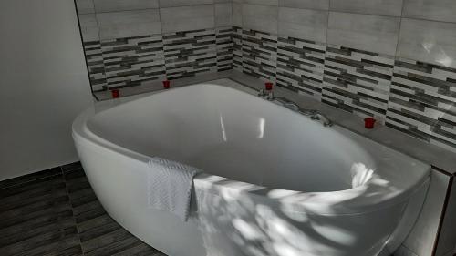 uma banheira branca na casa de banho com uma parede de azulejos em Arcanum Apartman em Makó