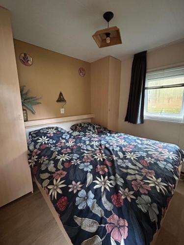 ein Schlafzimmer mit einem Bett mit geblümter Tagesdecke in der Unterkunft Fijne caravan midden in de bossen van de Veluwe in Hoenderloo